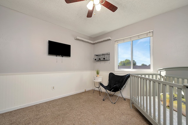 bedroom featuring light colored carpet, ceiling fan, a nursery area, and a textured ceiling