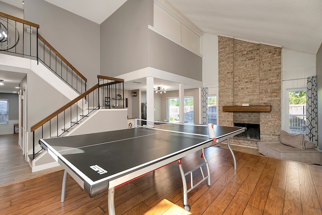 rec room with a stone fireplace, light wood-type flooring, high vaulted ceiling, and a healthy amount of sunlight