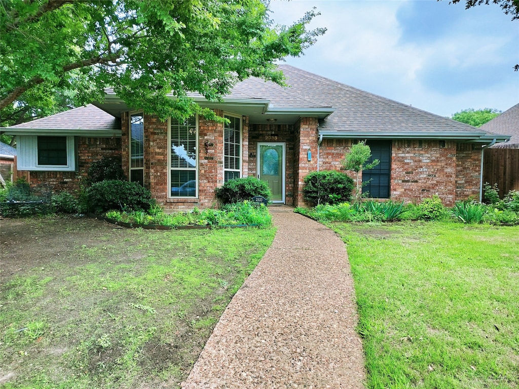 ranch-style home with brick siding, a shingled roof, and a front yard