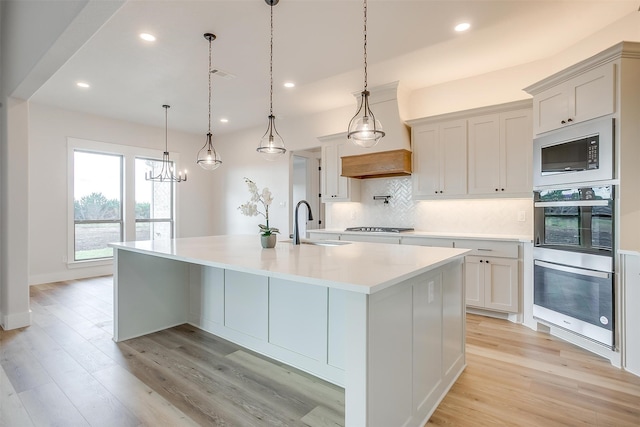 kitchen with premium range hood, appliances with stainless steel finishes, pendant lighting, light stone countertops, and sink