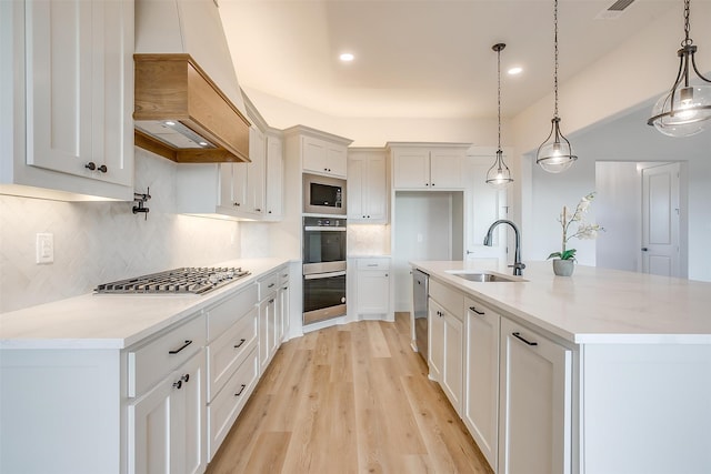 kitchen featuring stainless steel appliances, white cabinets, sink, an island with sink, and pendant lighting