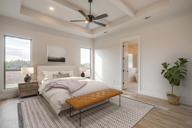 bedroom with light hardwood / wood-style floors, ceiling fan, connected bathroom, and a tray ceiling