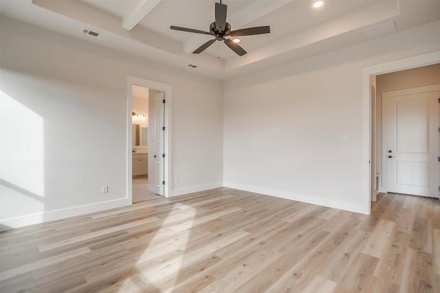 empty room with ceiling fan, a tray ceiling, and light hardwood / wood-style floors