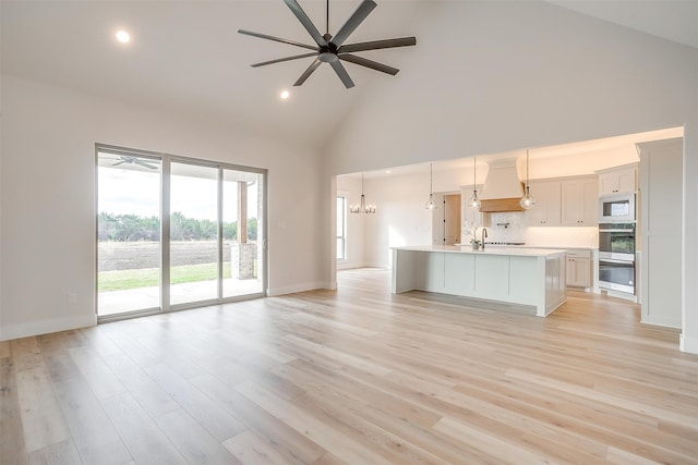 kitchen with high vaulted ceiling, pendant lighting, light wood-type flooring, and a kitchen island with sink