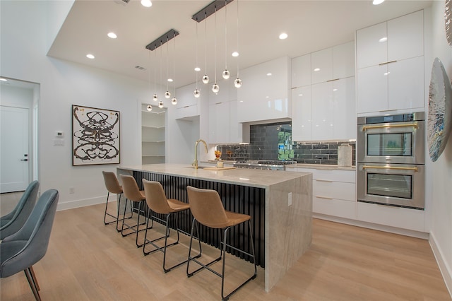 kitchen featuring appliances with stainless steel finishes, white cabinets, pendant lighting, light hardwood / wood-style flooring, and a kitchen island with sink