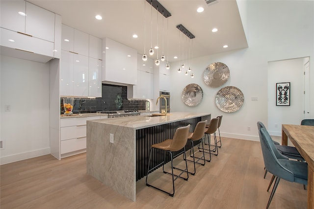 kitchen with light hardwood / wood-style floors, a breakfast bar area, white cabinetry, decorative backsplash, and decorative light fixtures