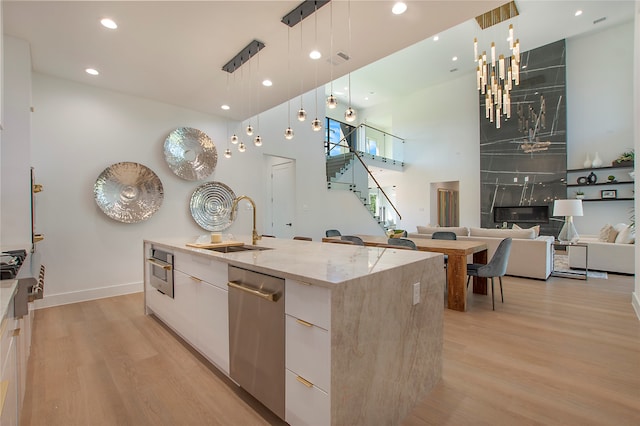 kitchen featuring white cabinets, decorative light fixtures, a large island with sink, stainless steel appliances, and light hardwood / wood-style floors