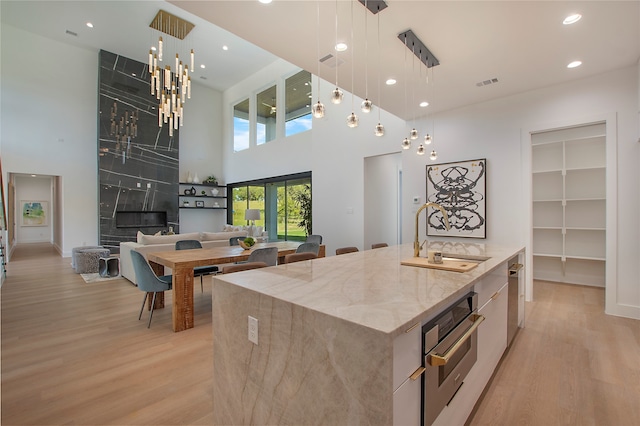 kitchen featuring pendant lighting, a kitchen island with sink, sink, light stone countertops, and stainless steel oven