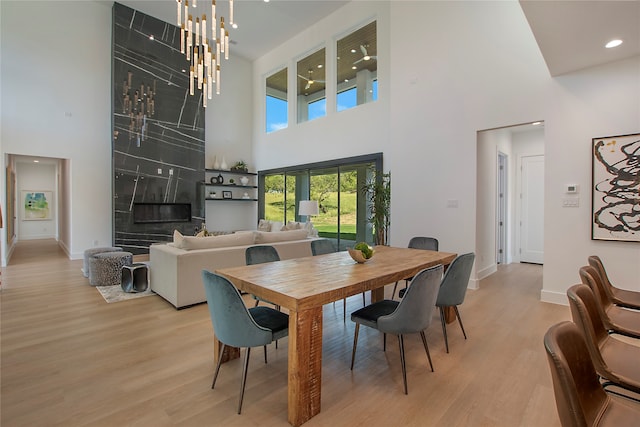 dining area featuring a notable chandelier, a towering ceiling, light hardwood / wood-style floors, and a premium fireplace