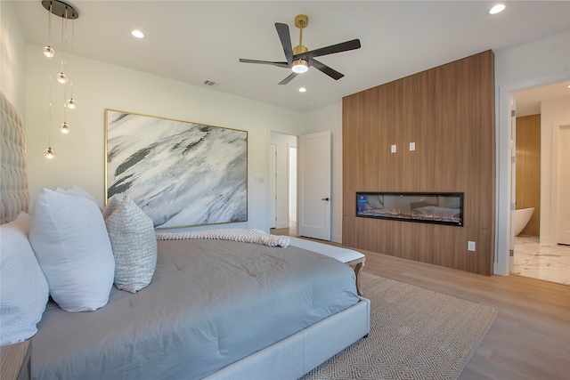 bedroom featuring a fireplace, ceiling fan, and light hardwood / wood-style flooring