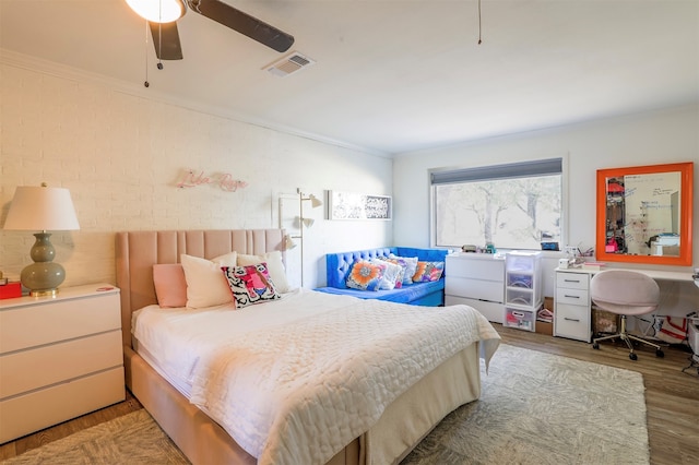 bedroom with ceiling fan, crown molding, brick wall, and wood-type flooring