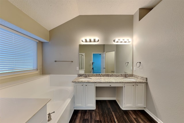 bathroom featuring vanity, a textured ceiling, hardwood / wood-style floors, lofted ceiling, and a bathing tub