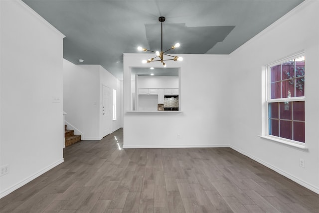 unfurnished living room with a notable chandelier, light wood-type flooring, and ornamental molding