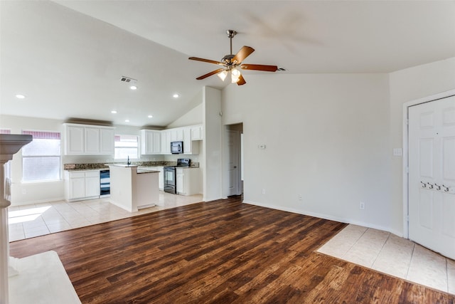 unfurnished living room with ceiling fan, sink, wine cooler, high vaulted ceiling, and light wood-type flooring