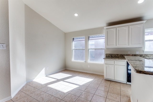 kitchen with white cabinetry, light tile patterned floors, dark stone counters, and lofted ceiling