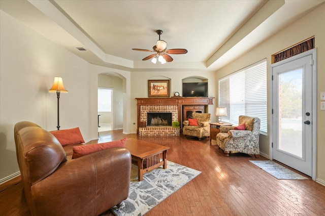 living room featuring a tray ceiling, a fireplace, ceiling fan, and hardwood / wood-style floors