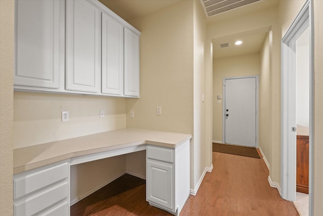 unfurnished office featuring built in desk and hardwood / wood-style flooring