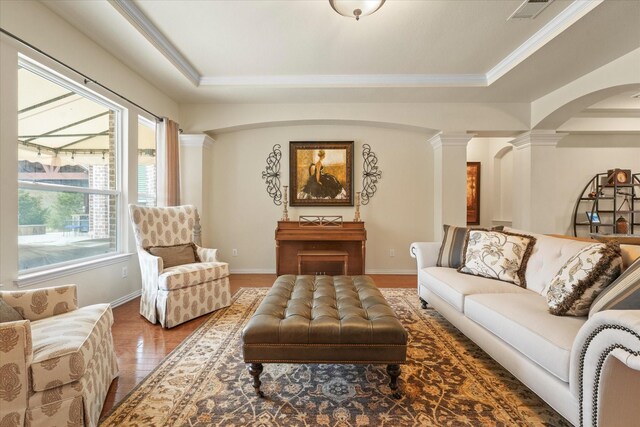 living room featuring hardwood / wood-style floors, ornamental molding, a tray ceiling, and decorative columns