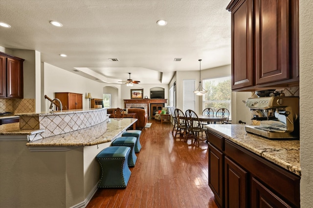 kitchen with a breakfast bar, ceiling fan, a fireplace, dark hardwood / wood-style floors, and hanging light fixtures