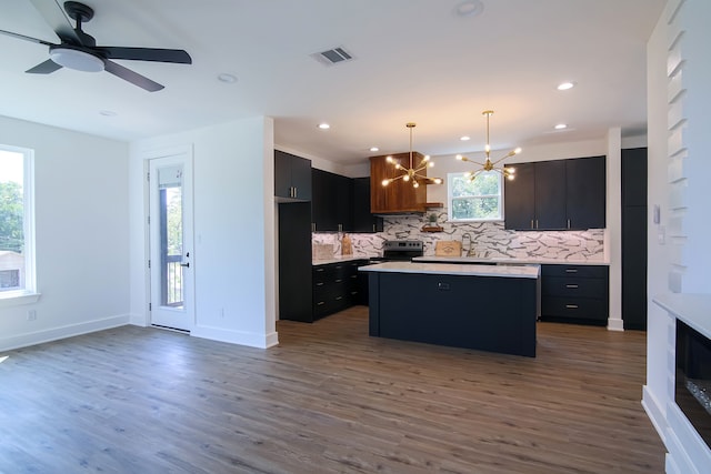 kitchen featuring decorative backsplash, dark hardwood / wood-style flooring, stainless steel stove, a kitchen island, and hanging light fixtures