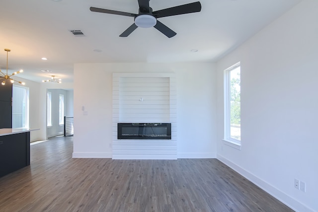 unfurnished living room featuring ceiling fan with notable chandelier, dark hardwood / wood-style flooring, and a fireplace