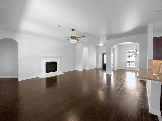 unfurnished living room featuring ceiling fan with notable chandelier and dark wood-type flooring