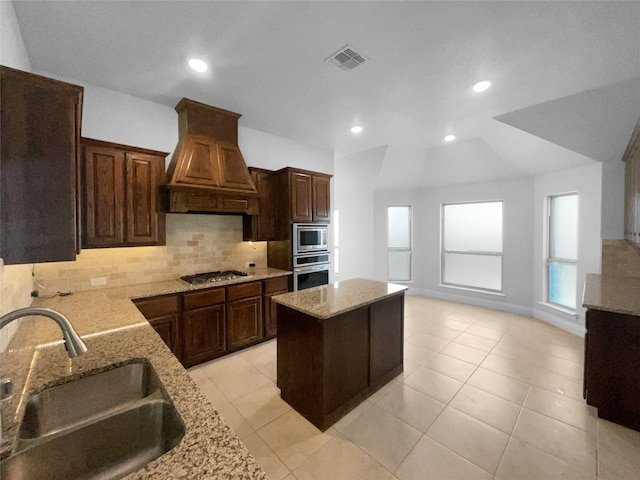 kitchen featuring light stone counters, sink, a kitchen island, custom exhaust hood, and appliances with stainless steel finishes