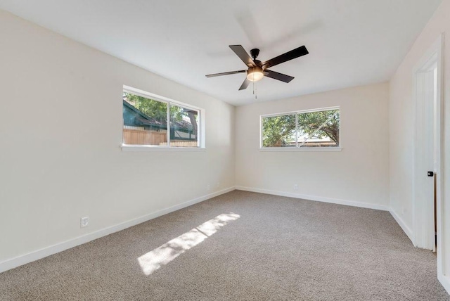 carpeted spare room featuring baseboards and a ceiling fan