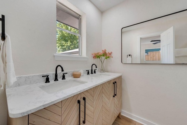 full bathroom with double vanity, baseboards, a sink, and wood finished floors