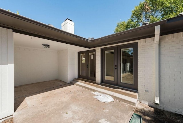 view of exterior entry with brick siding, a patio, and french doors