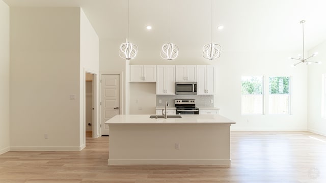 kitchen with light hardwood / wood-style floors, sink, white cabinets, stainless steel appliances, and a center island with sink