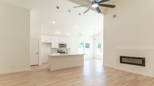 kitchen featuring an island with sink, light hardwood / wood-style flooring, white cabinetry, appliances with stainless steel finishes, and ceiling fan with notable chandelier