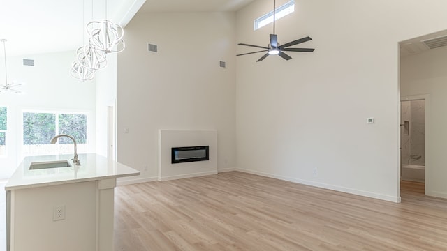 unfurnished living room with ceiling fan, light wood-type flooring, sink, and high vaulted ceiling