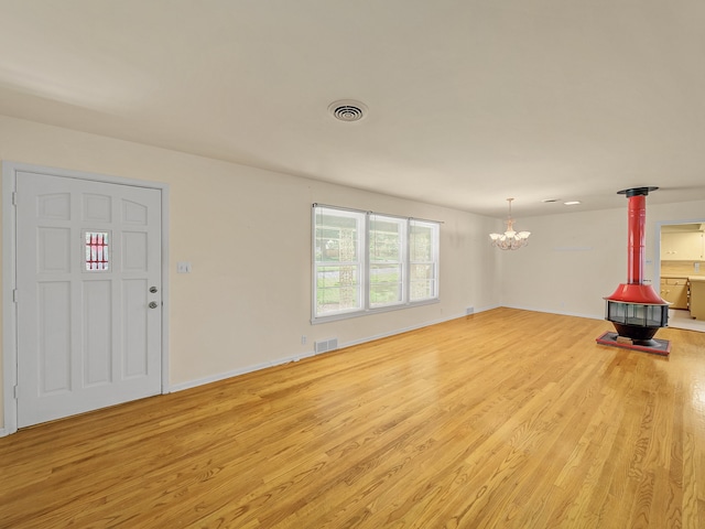 unfurnished living room featuring light hardwood / wood-style flooring, a wood stove, and a notable chandelier