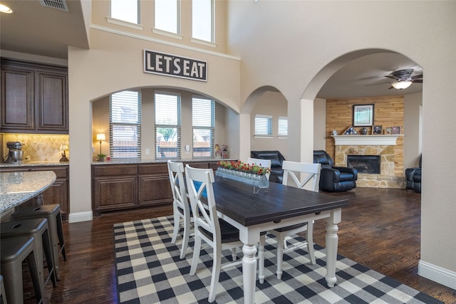 dining room featuring ceiling fan, a stone fireplace, dark hardwood / wood-style flooring, and wood walls