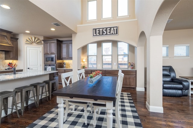 dining area featuring a high ceiling, plenty of natural light, sink, and dark hardwood / wood-style flooring