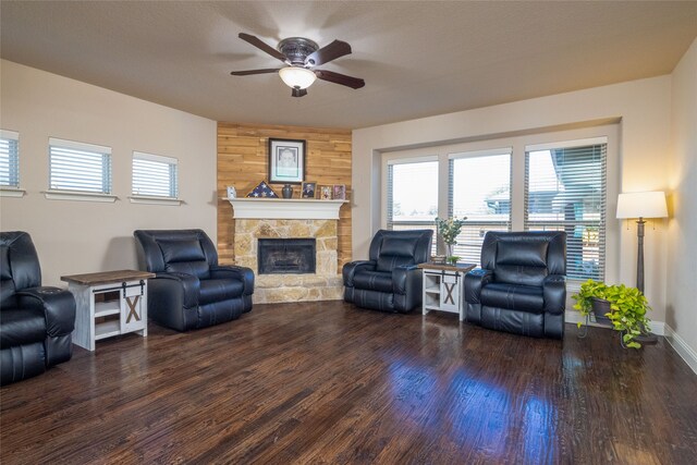 living room featuring a stone fireplace, dark hardwood / wood-style floors, wooden walls, and ceiling fan