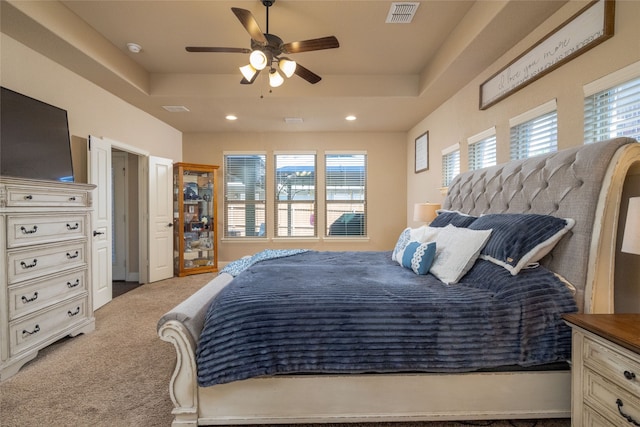 bedroom featuring ceiling fan, light colored carpet, and a tray ceiling