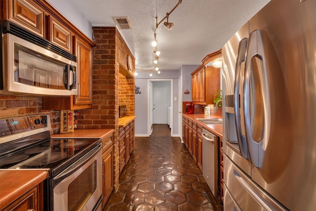 kitchen with dark tile patterned floors, stainless steel appliances, a textured ceiling, and sink