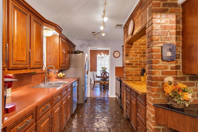 kitchen with sink, dark tile patterned floors, a textured ceiling, track lighting, and dishwasher