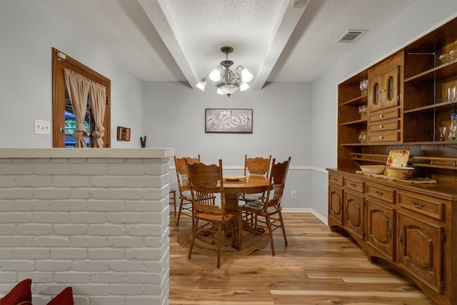 dining area with a textured ceiling, light wood-type flooring, beam ceiling, and a chandelier