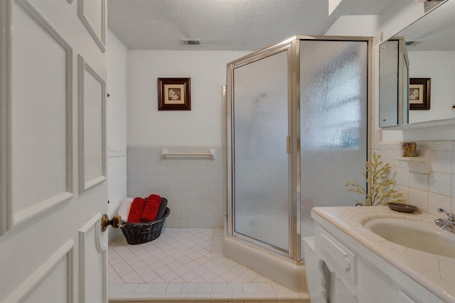 bathroom with vanity, tile walls, a textured ceiling, and a shower with door