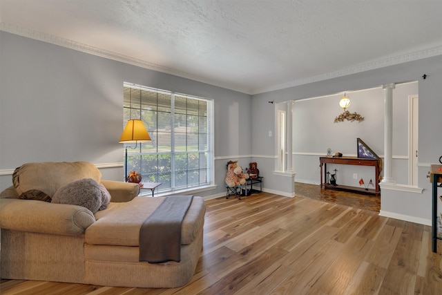 living area featuring a textured ceiling, hardwood / wood-style flooring, crown molding, and ornate columns