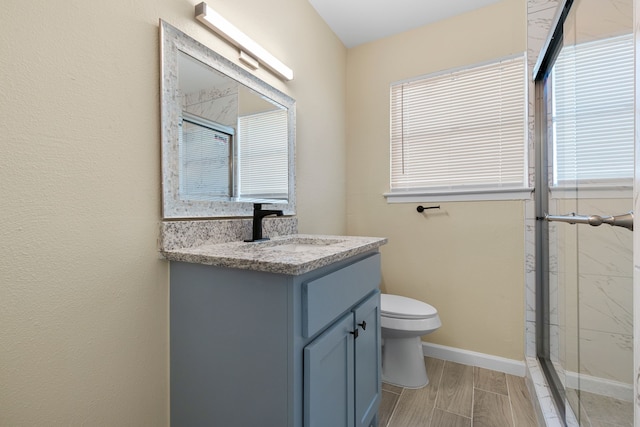 bathroom with a wealth of natural light, a shower with shower door, vanity, and toilet