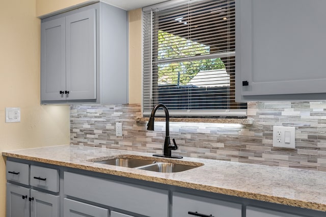 kitchen featuring backsplash, gray cabinetry, sink, and light stone countertops