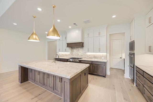 kitchen featuring backsplash, decorative light fixtures, white cabinets, light hardwood / wood-style flooring, and a center island with sink