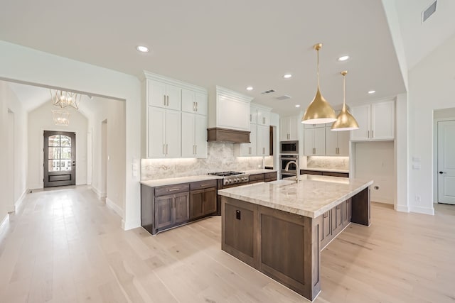 kitchen with light hardwood / wood-style floors, white cabinetry, stainless steel appliances, and a center island with sink