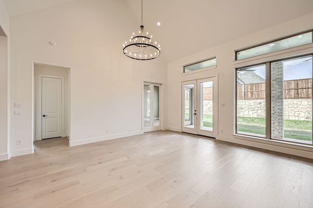 unfurnished room with an inviting chandelier, light hardwood / wood-style flooring, and high vaulted ceiling