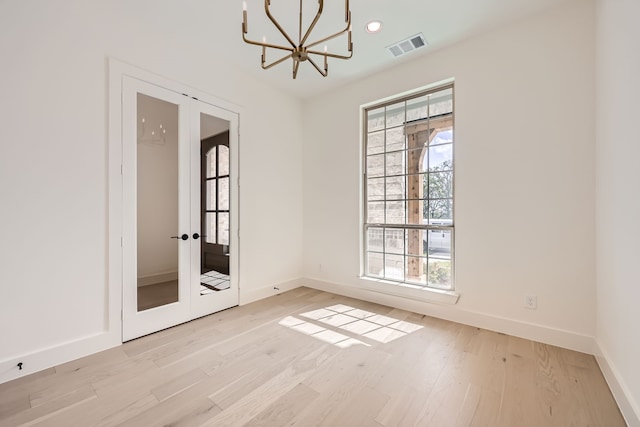 empty room with a chandelier, french doors, and light wood-type flooring