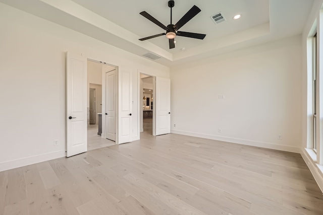 unfurnished bedroom featuring a tray ceiling, light wood-type flooring, and ceiling fan